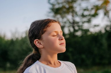 Açık havada tatlı, rahat küçük bir çocuğun portresi sıcak günbatımında doğadan temiz hava soluyor. Yeşil Park 'ın keyfini çıkartan güzel bir kıza yakın durun. Çocukluk kavramı