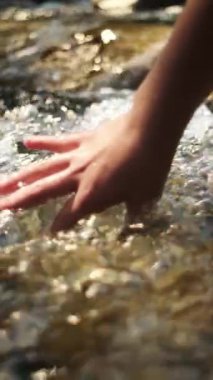 Güneşli bir yaz gününde vahşi dağların su yüzeyine dokunan çocuk eliyle ilgili dikey video. Doğayla barışçıl ve düşünceli bir bağ. Meditasyon ilhamını kabul et. Yavaş çekim