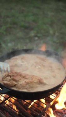 Tavada domates ve peynir soslu tavuk eti pişiren kimliği belirsiz genç bir kadının dikey videosu. Sonbahar akşamı sıcak kamp ateşi üzerinde yemek pişirmek. Yemek, macera ve tatil doğa konsepti