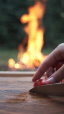 Yazın veya sonbahar akşamları kamp ateşinin yanında tahta tahtada taze kırmızı domates kesen bıçak kullanan kadınların dikey görüntüleri. Sağlıklı beslenme. Dilimlenmiş domates. Kamp kavramı