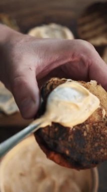Dışarıdaki tahtadan bir tahtanın üzerinde hamburger hazırlayan genç adamın dikey videosu. Erkek eli, hamburger için kızarmış hamburger sosu sürer. Yemek pişirme doğa konsepti