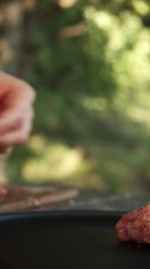 Delikanlının dikey görüntüsü, açık havada hamburger için kıymalı pirzola yapıyor. Erkek elleri çiğ eti karıştırır ve tabağa koyar. Doğa konseptinde yemek pişirmek