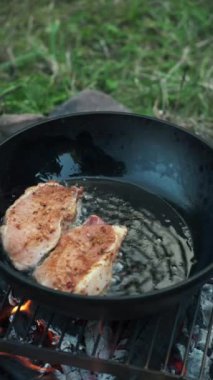 Genç bir adamın kamp ateşinde dumanla biftek pişirişinin dikey görüntüleri. Doğada barbekü. Şenlik ateşinde yemek pişirmek. Macera, seyahat ve yürüyüş kavramı