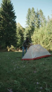 Maceralı çadır kuran, seyahat eden ve ormanda tatil yapmak için doğada dinlenen genç bir adamın dikey görüntüleri. Barınak, güvenlik ve kamp alanı, yürüyüş ve açık hava tatili konsepti
