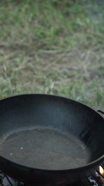 Erkek elinin dikey videosu yaz ya da sonbahar günü kamp ateşinde tavaya zeytinyağı döker. Dinlenme ve piknik konsepti. Yemek pişirme konsepti. Kamp yaşam tarzı rutini