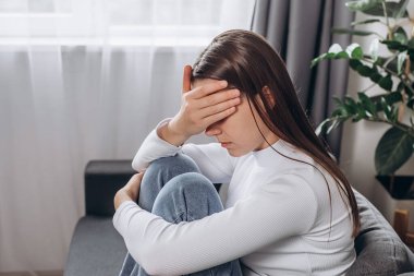 Endişeli, genç, beyaz bir kadın, evde tek başına oturmuş, düşünen, endişeli, mutsuz, esmer kadın, psikolojik problemler yaşıyor, yas tutuyor ya da konsept özlemi çekiyor.