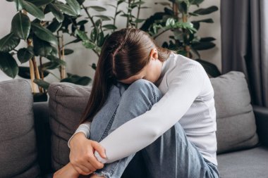 Mutsuz kaygılı genç bir kadın diziyle yüzünü kapatıyor. Oturma odasında tek başına oturuyor. Kalbi kırık depresyondaki bir kadın.