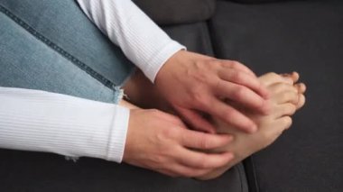 Ayak ağrısı konsepti. Genç bir kadının el kaşıması, ayak kaşıntısı, evdeki koltukta kaşınan cilt, mantar iltihabı, mantar bakteri enfeksiyonu, alerjik reaksiyon, egzama.