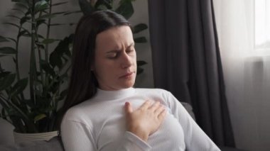 Kalp krizi, sağlık konsepti. Göğüs ağrısına dokunan akut kardiyak genç beyaz kadın eli, kadın solunum problemi, evdeki kanepede tek başına oturan baskı.