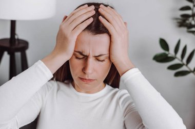 Stresli genç bir kadının kafasına dokunması baş dönmesi, baş ağrısı ve migren ağrısı, evdeki kanepede yalnız başına oturması, yorgun ve bitkin bir bayanın kendini kötü hissetmesi. Kriz kavramı