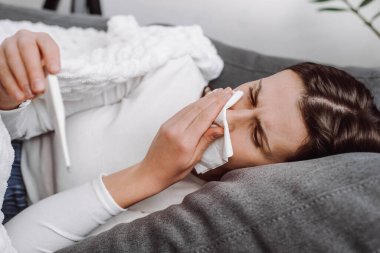 Hasta, üzgün, genç bir kadının evdeki kanepede uzanmış termometreyle mücadele etmesi, kendini kötü hissetmesi, soğuk algınlığı geçirmesi, beyaz bir kadının gribe yakalanması.