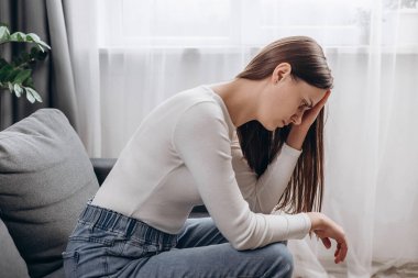 Endişeli genç beyaz kadın kanepeye tek başına oturmuş, umutsuz kadın hayatı, sağlığı ya da duygusal sorunu düşünüyor, üzgün hissediyor, anksiyete konseptinden acı çekiyor.