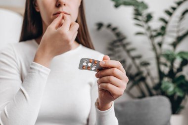 Kafkasyalı genç bir kadının elinde küçük bir tıbbi hap tutarak koltuğa oturması, cilt, saç ve tırnak güçlendirme tedavisi için C vitamini alması ya da yemesi. Beslenme takviyesi kavramı
