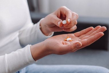 Kanepede oturan kadın el haplarını, mide ağrısı, baş ağrısı, tedavi için ağrı kesicileri, evde ilaç veya vitamin almayı, sağlık hizmetleri kavramını,
