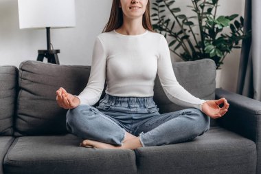 Mutlu genç kadın elleri rahat bir şekilde poz veriyor Lotus pozisyonunda meditasyon yapıyor evdeki rahat koltukta, rahatlıyor, refah için egzersiz yapıyor. Meditasyon konsepti. Rahatlama, mutlu eğlence insanları.