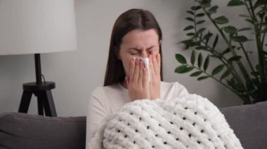 Coronavirus ya da Cvid-19 konsepti. Sağlıksız, hasta, genç bir kadının ateşi, nezlesi ve kullandığı mendiller hapşıran burnu, evde tek başına kanepede otururken akan bir burnu vardır. Virüslü şahsın sağlık hizmeti