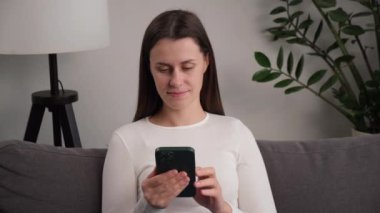 Evdeki rahat koltukta oturan, akıllı telefon kullanan mutlu, beyaz bir kadın. Gülümseyen tatlı kız cep telefonu ve mesaj atıyor. Teknoloji, girişim, yeni iş ve iletişim kavramı