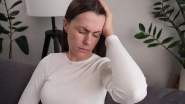 Yorgun, genç bir kadın. Stres baş ağrısı. Evdeki kanepede otururken depresyona giriyor. Hüzünlü kadın baş ağrısı rahatsız edici migren aşırı çalışma bıkkınlık endişe endişe endişe sorun
