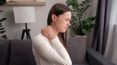 Mutsuz, genç, beyaz bir kadın masaj yapıyor omuzlarını ovuyor, kaslarını geriyor, yorgun, eklem ağrısı çekiyor evde tek başına oturuyor. Fibromiyalji kavramı