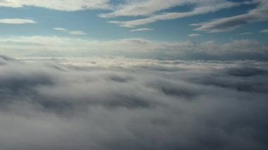 Kışın beyaz bulutların ve mavi gökyüzünün havadan görünüşü. İHA kabarık bulutların arasından gökyüzüne doğru uçuyor. Doğa konsepti. Dramatik sahne