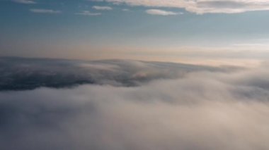 Hareket eden beyaz bulutlar mavi gökyüzü manzaralı hava manzarası. Drone kışın sabah vakti mavi gökyüzünde kabarık bulutların arasından geri uçar. Güneş, gün doğumundaki siste bulutların arkasında gizlidir. Doğa konsepti