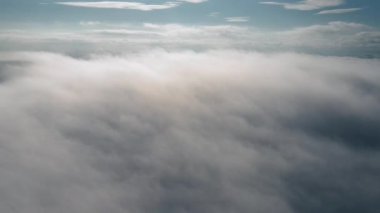 Drone kışın sabah vakti mavi gökyüzünde kabarık bulutların arasından geri uçar. Hareket eden beyaz bulutlar mavi gökyüzü manzaralı hava manzarası. Güneş, gün doğumundaki siste bulutların arkasında gizlidir. Doğa konsepti