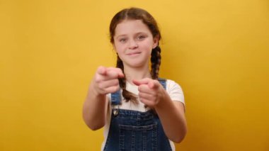 Sevimli genç kız işaret parmağı kamerasının portresi. Stüdyoda sade sarı arka plan duvarında izole bir şekilde poz veriyor. Çocukluk yaşam tarzı konsepti