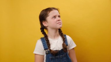 Stüdyodaki sarı arkaplan duvarında izole edilmiş bir şekilde duran, işaret parmağıyla işaret parmağını kaldıran sevimli, gülümseyen genç kız portresi. Çocukluk kavramı