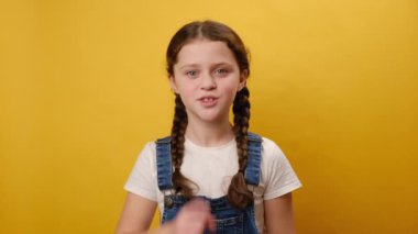 Stüdyodaki sarı renkli arka plan duvarında izole edilmiş bir poz vererek sessiz olun diyen küçük kız çocuğunun portresi. Çocukluk yaşam tarzı konsepti
