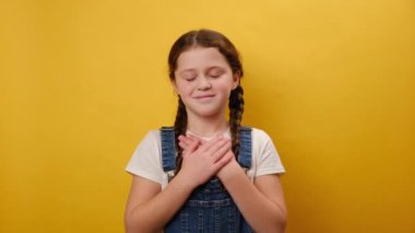 Sevimli, gülümseyen çocuk portresi kalp işaretinin üzerine katlanmış eller koydu. Stüdyodaki sarı arka plan duvarında izole bir şekilde poz verdi. Çocukluk yaşam tarzı konsepti