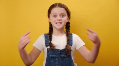 Stüdyodaki sarı renkli arka plan duvarında izole bir şekilde poz veren mutlu, gülümseyen, çocukluk çağındaki kız çocuk işaret fişeği portresi. Çocukluk yaşam tarzı konsepti