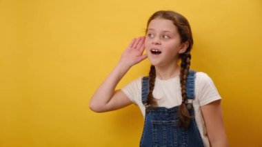 Meraklı küçük kız çocuğunun portresi dikkatle dinlediğini duymaya çalışıyor, stüdyodaki sarı arka plan duvarında izole edilmiş poz veriyor. Çocukluk yaşam tarzı konsepti