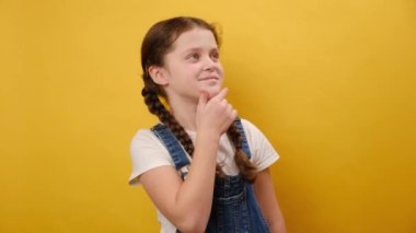 Mutlu, çocukluk çağındaki güzel bir kızın portresi. Çene kenarına bakıyor. Stüdyodaki sarı arka plan duvarında izole bir şekilde duruyor. Çocukluk yaşam tarzı konsepti