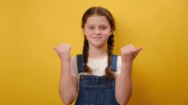 Çocuk yaşta gülümseyen güzel bir kızın portresi başparmağıyla fotokopi alanının maketini yapıp stüdyodaki sade sarı arka plan duvarının üzerinde izole bir poz veriyor. Çocukluk yaşam tarzı konsepti
