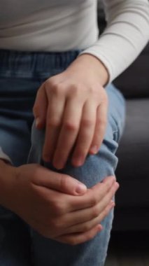 Genç beyaz kadının bacağına dokunduğu diz eklemlerinde ağrı hissettiği ve iltihap ve ağrıdan dolayı düzgün yürüyemediği dikey bir video. Artrit kronik hastalık sorunu kavramı