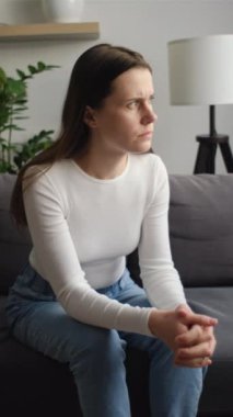 Endişeli beyaz bir kadının kanepede yalnız başına oturmasının dikey görüntüsü umutsuz bir kadının hayatı, sağlığı ya da duygusal sorunu düşünmesi, üzgün hissetmesi, endişe konseptinden muzdarip olması.