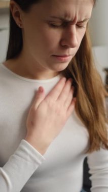 Kanepede tek başına otururken göğüs ağrısı çeken sağlıksız genç beyaz bir kadının dikey görüntüsü. Üzgün kadın evinde kalp ağrısı, enfarktüs ya da kalp hastalığı konsepti yüzünden acı çekiyor.