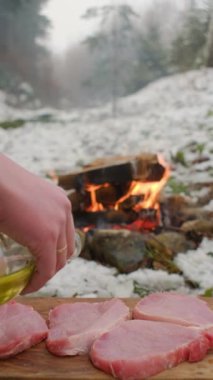 Şenlik ateşinin yanındaki kış ormanında pişirmeden önce aşçının dikey videosu taze etin üzerine bol bol yağ döker. Yağ yemek için sululuk ve lezzet sağlar, aynı zamanda hassasiyetini korur. Yemek pişirme konsepti