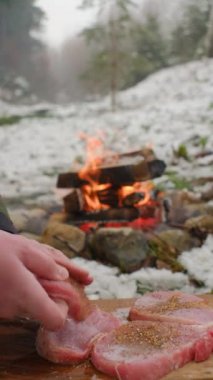 Genç adamın dikey videosu, kış zamanı şenlik ateşinin yanında marine edilmiş et. Yemek pişirmeye hazırlanıyorum. Kamp ortamı ve açık hava yaşam tarzı konsepti
