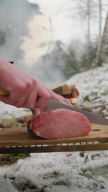 Erkek ellerinin dikey videosu kamp yaparken ya da kış zamanı yürüyüş yaparken yemek pişirmek için şenlik ateşinin yanında taze et hazırlıyor. Açık hava pişirme konsepti