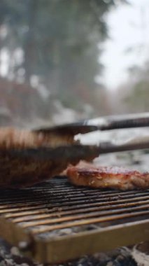 Bilinmeyen bir gencin kış ormanında şenlik ateşinde biftek metal ızgara pişirirken çekilmiş dikey görüntüleri. Şenlik ateşinde yemek pişirmenin en iyi manzarası. Kamp ortamı ve açık hava yaşam tarzı konsepti
