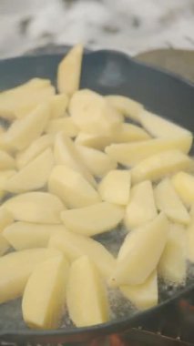 Kış günü kızarmış patates pişirirken çekilmiş dikey bir video. Yürüyüşte dışarıda yemek pişirmek. Yiyecek konsepti