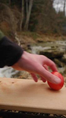 Erkek ellerinin dikey videosu Spring dağları nehri yakınlarındaki tahta tahtada domatesleri parçalara ayırıyor. Genç adam domatesleri doğaya bıçakla kesti. Yemek pişirme konsepti