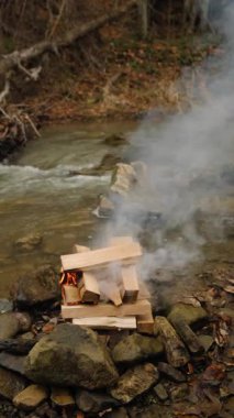 Kışın veya ilkbaharın başında dağların yanındaki kamp ateşinin dikey görüntüleri. Sakin şenlik ateşi, yanan odun. Aktif yaşam tarzı, seyahat, yürüyüş. Kamp havası ve açık hava yaşam tarzı.