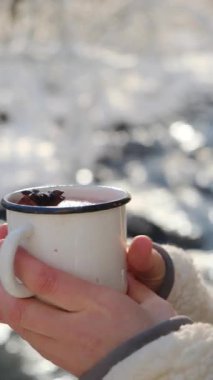 Muhteşem kış nehrinin yanında şarap içen mutlu genç bir kadının dikey videosu. Rahat kız sihirli doğada sıcak içeceğin tadını çıkarıyor. Güzel gülümseyen bayan bardaktan yudumluyor açık havada dinleniyor