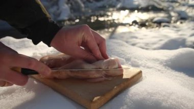 Erkek eli yemek pişirirken yakın çekim dağların yanındaki nehirde tahta tahtada tavuk kesiyor. Sağlıklı yiyecekler. İnsanlar kamp yapıyor ve dışarıda yemek pişiriyor.