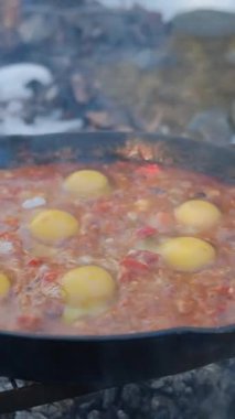 Şenlik ateşinde Shakuka pişirirken çekilmiş dikey görüntüler. Sağlıklı taze sebzeler. Çeşitli sebzeler. Vejetaryen yemeği. Kamp ortamı, açık hava yaşam tarzı konsepti.