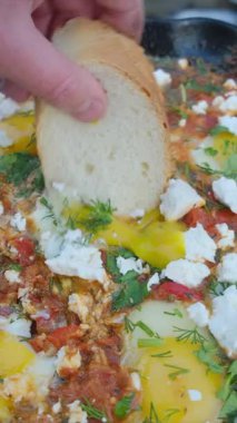 Erkek elini sarısına daldırır ve kış zamanı arka plandaki vahşi nehirde kendini gösterir. Shakshuka yumurtaları, domates, büyük taşta sıcak tavada biber. Kamp ortamı, açık hava yaşam tarzı konsepti.