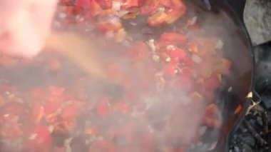 Kimliği belirsiz genç adam, şenlik ateşinde sebzeleri karıştırıyor. Spagetti bolonez için sos ya da tavada tahta kaşıkla pizza yapmak. Yemek pişirme konsepti