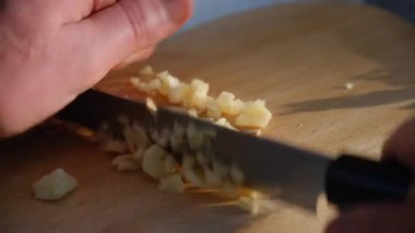 Kış günü tahta tahtada sarımsak doğrayan tanınmamış erkek elleri. Adamın elleri sarımsağı doğaya bıçakla kesiyor. Yemek pişirme konsepti